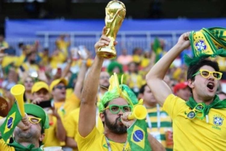 Torcida brasileira com uniformes amarelo e verde celebrando a Taça da Copa do Mundo FIFA erguida